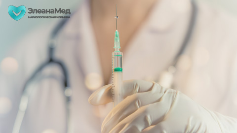 Рука врача в медицинской перчатке держит шприц